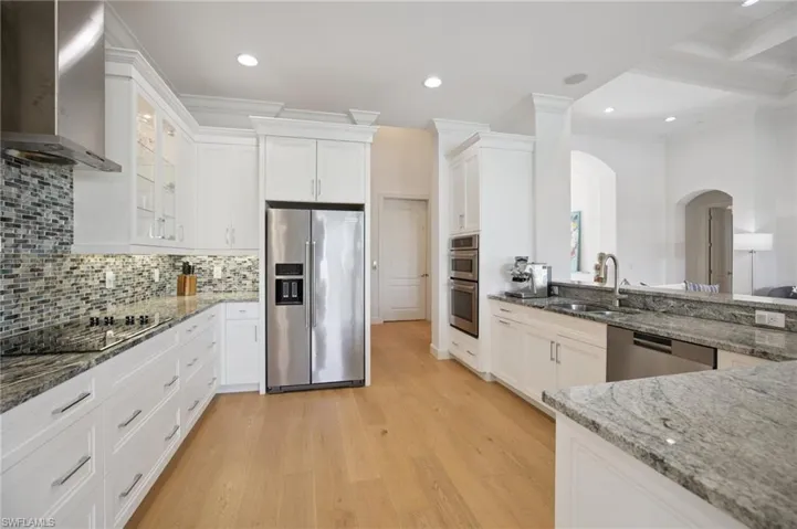 The kitchen has stainless steel appliances, spacious  counter space, white cabinets, attractive backsplash, and wood floor
