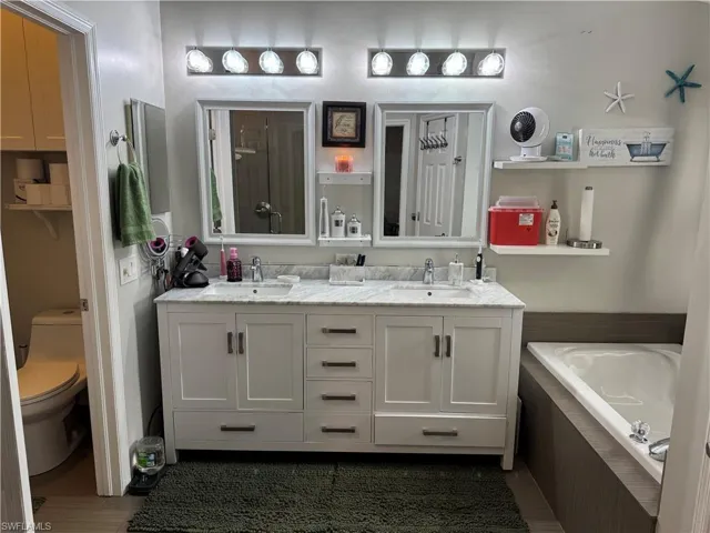 Bathroom with double vanity, a bath, and dark wood-style floors