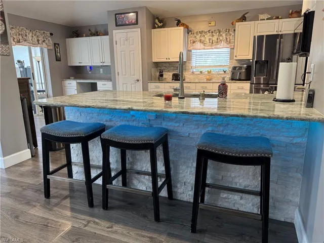 Kitchen with white cabinets, a peninsula, stainless steel fridge with ice dispenser, and light stone counters