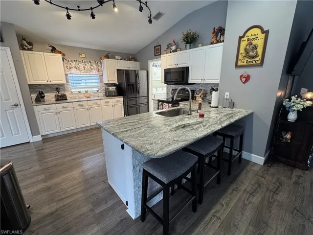 Kitchen with decorative backsplash, a breakfast bar area, black appliances, dark wood-style floors, and vaulted ceiling