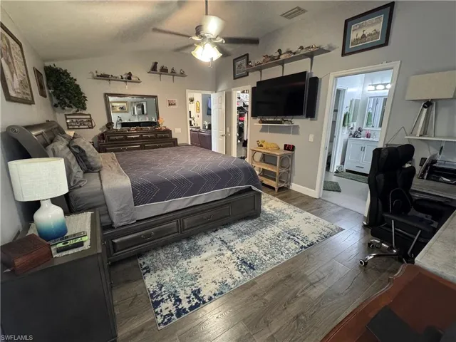 Bedroom with ensuite bathroom, wood finished floors, vaulted ceiling, a walk in closet, and a ceiling fan