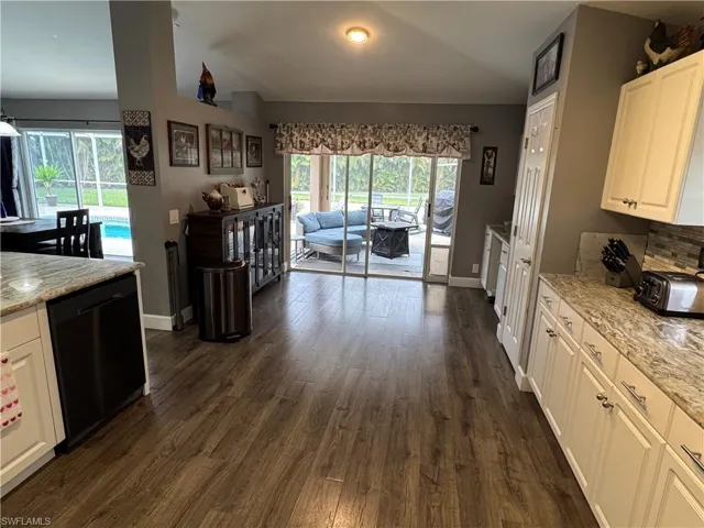 Kitchen featuring white cabinetry, light stone countertops, black dishwasher, vaulted ceiling, and dark wood-type flooring