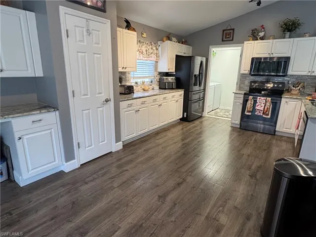 Kitchen with appliances with stainless steel finishes, light stone counters, tasteful backsplash, white cabinets, and dark wood-style flooring
