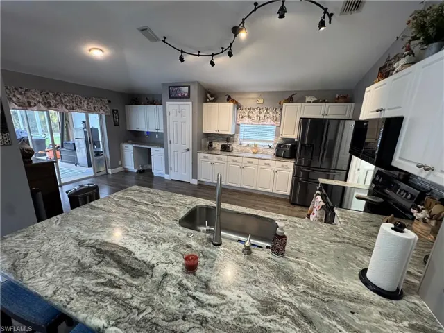 Kitchen featuring fridge with ice dispenser, lofted ceiling, plenty of natural light, white cabinetry, and dark wood finished floors