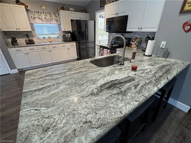 Kitchen featuring dark wood-style flooring, light stone counters, black appliances, a kitchen breakfast bar, and a peninsula