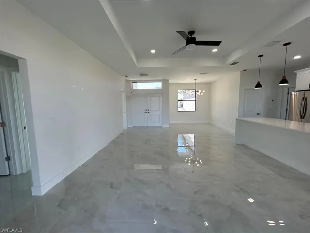 Unfurnished living room featuring ceiling fan, a raised ceiling, and suspended lighting