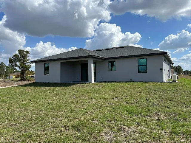 Rear view of property with stucco siding, a patio area, a lawn, and roof with shingles