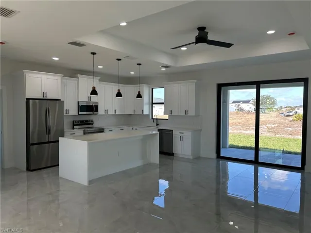 Kitchen with stainless steel appliances, white cabinets, a center island, ceiling fan, and a tray ceiling