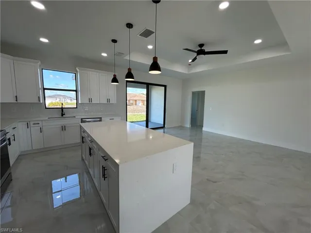 Kitchen featuring a kitchen island, white cabinetry, decorative light fixtures, ceiling fan, and light stone counters