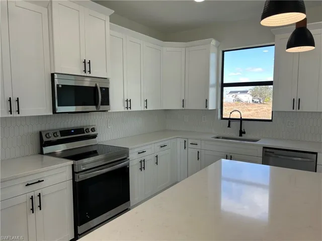 Kitchen featuring stainless steel appliances, white cabinets, tasteful backsplash, and light stone counters