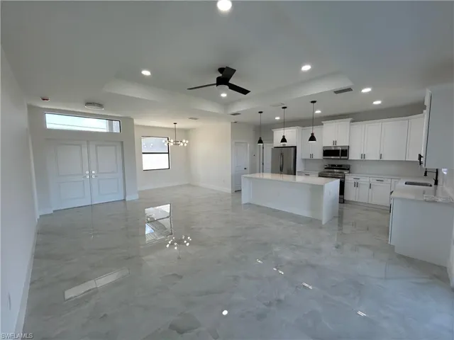 Kitchen with a raised ceiling, stainless steel appliances, ceiling fan, light marble finish flooring, and white cabinets