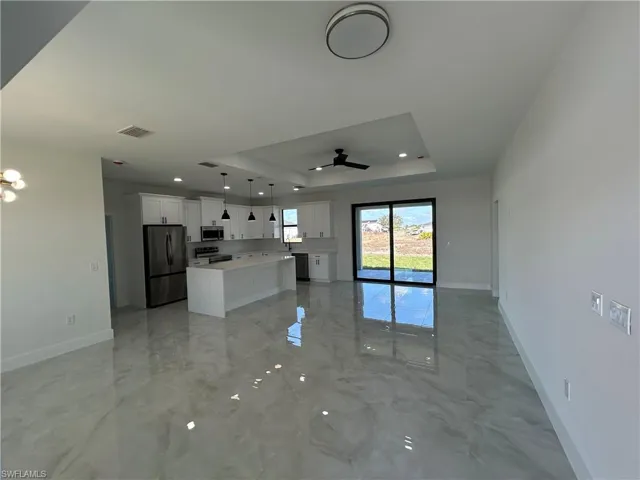 Kitchen with open floor plan, white cabinets, a kitchen island, a tray ceiling, and black appliances