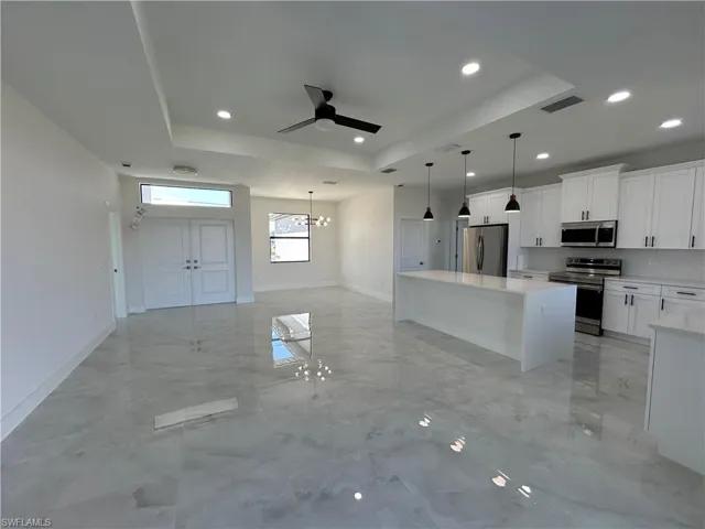 Kitchen featuring a raised ceiling, ceiling fan, stainless steel appliances, white cabinetry, and open floor plan