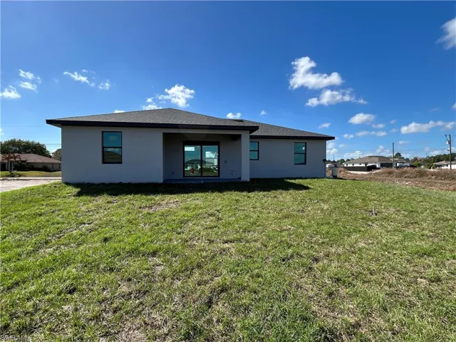 Rear view of house with stucco siding, a yard, a patio area, and a shingled roof
