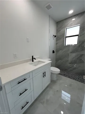 Full bath featuring vanity, tiled shower, light marble finish flooring, and recessed lighting