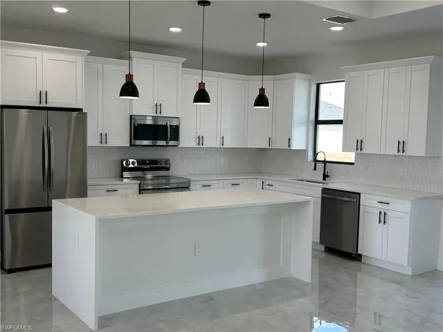 Kitchen featuring stainless steel appliances, a center island, light stone countertops, white cabinetry, and hanging light fixtures