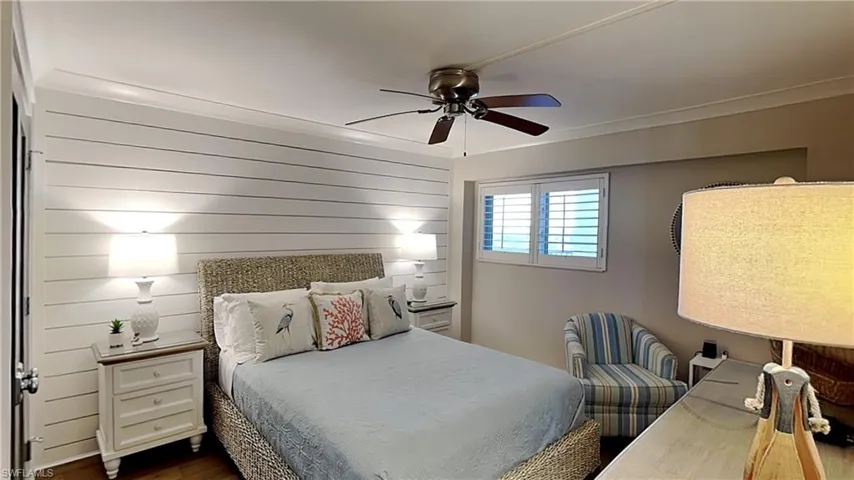 Bedroom featuring shiplap accent wall, crown molding, plantation shutters, and a ceiling fan