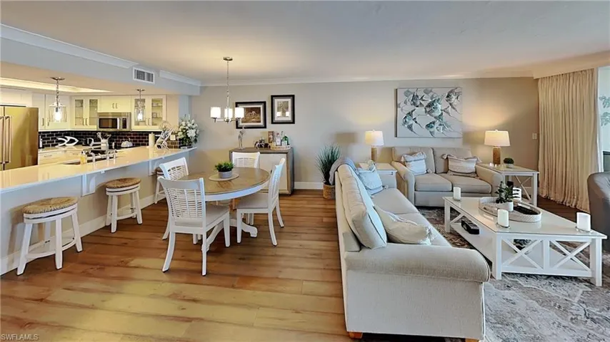 Spacious open-concept living area featuring wood-finish flooring, a kitchen island with seating, pendant lighting, and a dining area with a chandelier