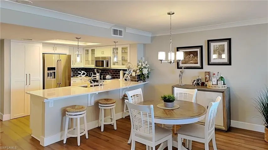 Kitchen featuring white cabinetry, stainless steel appliances, a white countertop, dark tile backsplash, and wood-finish flooring