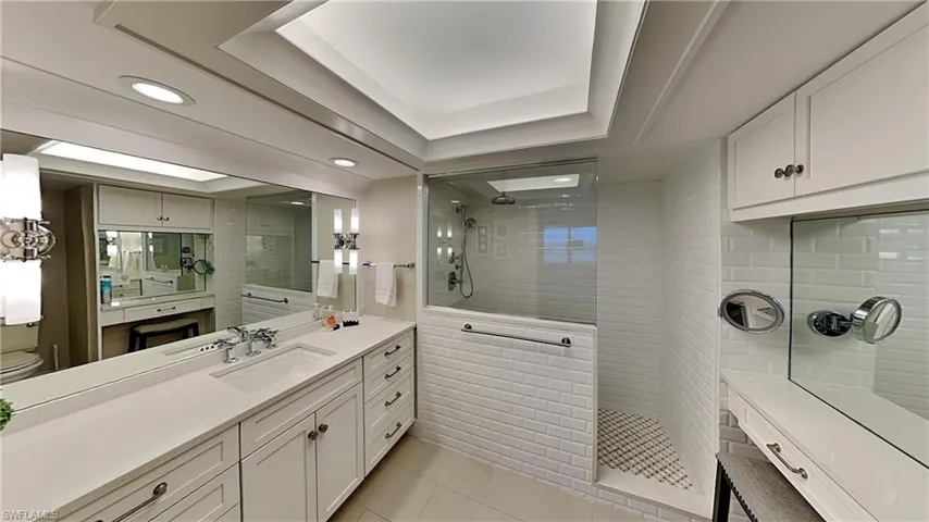 Spacious bathroom featuring an expansive vanity with double sinks, white shaker cabinetry, and a full-width mirror
