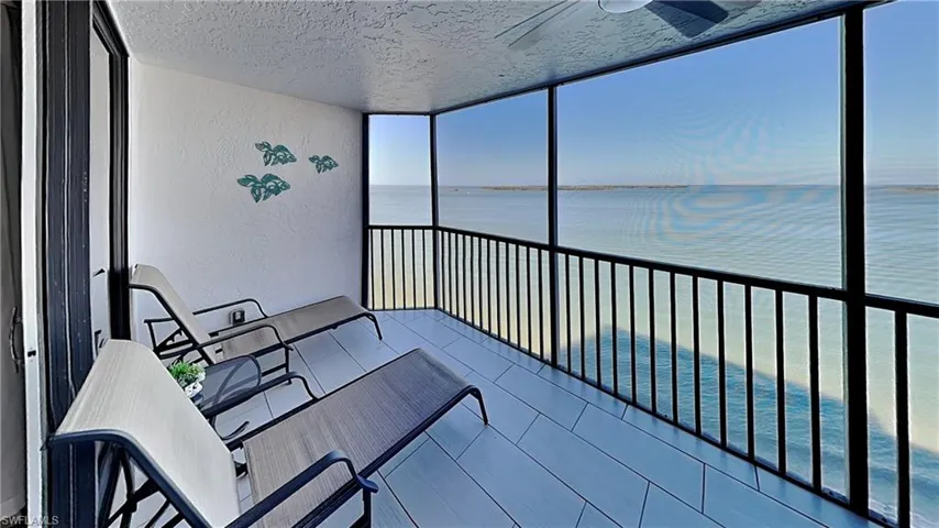 Screened balcony featuring expansive water scenery, textured walls, a ceiling fan, and light-toned tile flooring