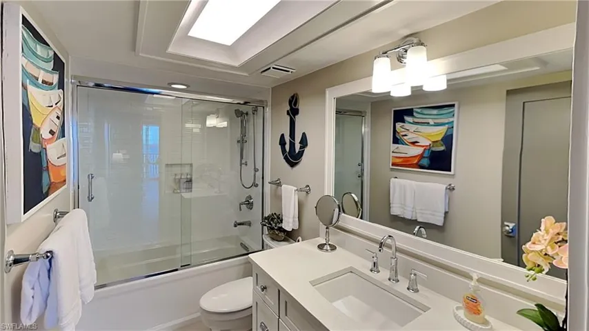 Bathroom featuring a single vanity with an integrated sink and light-toned countertop, a large framed mirror, a tub/shower combination with sliding glass doors, and recessed ceiling lighting
