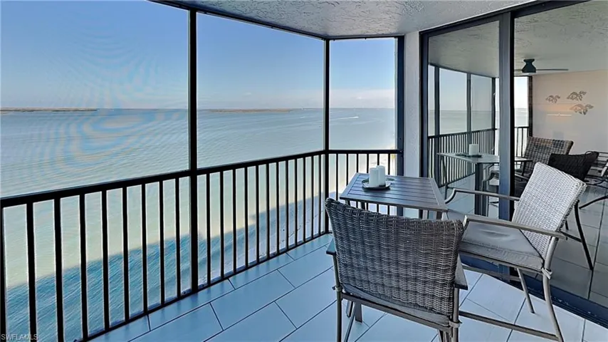 Screened balcony featuring expansive water scenery, tile flooring, black metal railings, and sliding glass doors