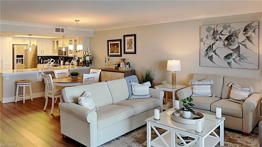 Open-concept living space featuring wood-finish flooring, recessed lighting, crown molding, and a kitchen with white cabinetry, stainless steel appliances, and pendant lighting over a breakfast bar