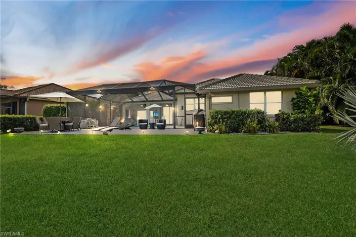 Back house at dusk with a lanai, a lawn, and a patio