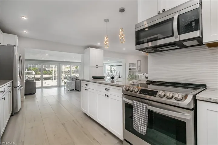 Kitchen featuring stainless steel appliances, light wood grain tile floors, light cabinetry and recessed lighting with custom style pendants over eating bar and light stone countertops with designer tile backsplash