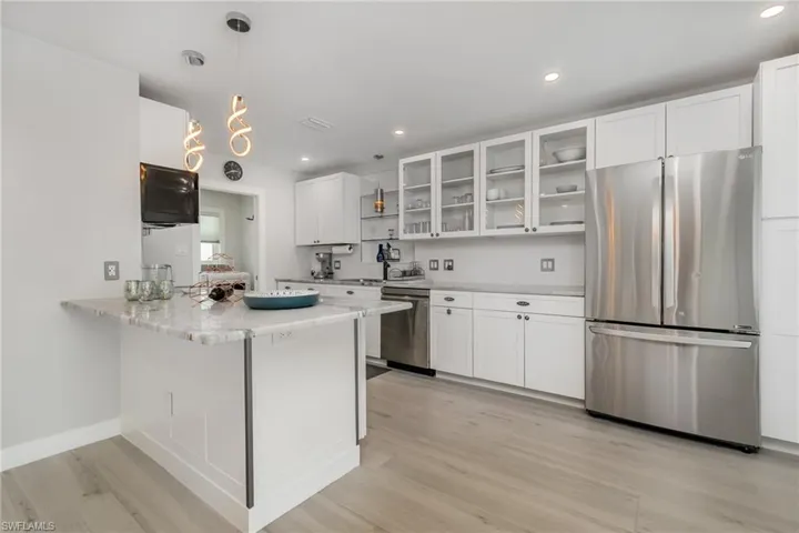 Kitchen featuring stainless steel appliances, light wood grain tile floors, light cabinetry, glass insert cabinets, and recessed lighting with custom style pendants over eating bar