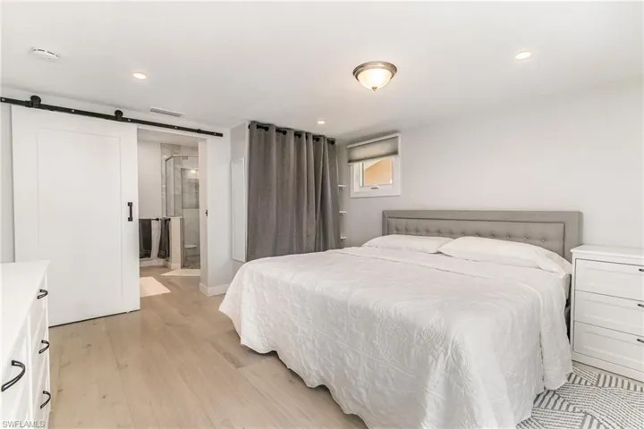 Primary Bedroom with light wood grain tile floors, a barn door, recessed lighting, baseboards, and ensuite bath