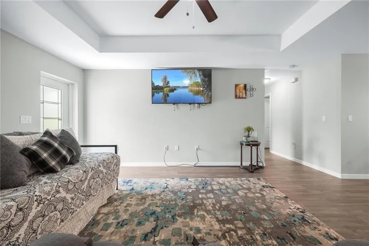 Living room with ceiling fan, a raised ceiling, and wood-type flooring