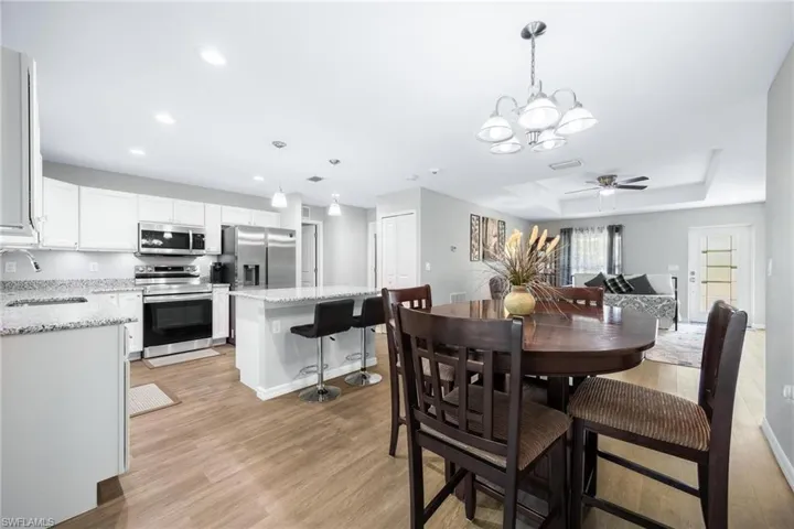 Dining space with light wood-type flooring, ceiling fan with notable chandelier, sink, and a tray ceiling