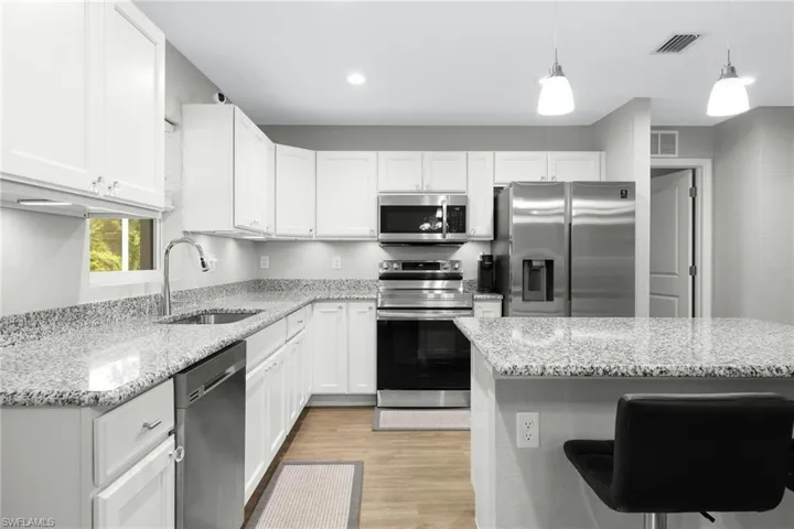 Kitchen with stainless steel appliances, sink, light stone counters, light wood-type flooring, and white cabinets
