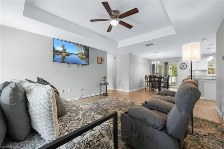Living room with ceiling fan with notable chandelier, a tray ceiling, and light wood-type flooring