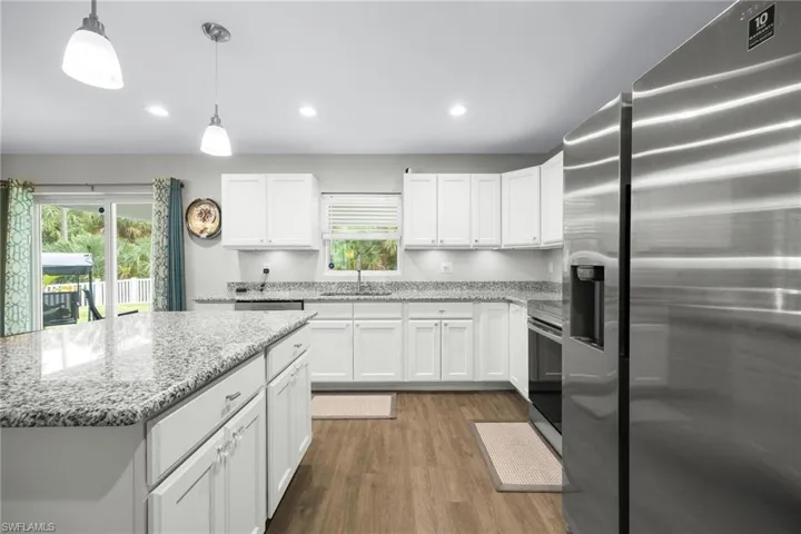 Kitchen featuring wood-type flooring, high quality fridge, pendant lighting, and a healthy amount of sunlight