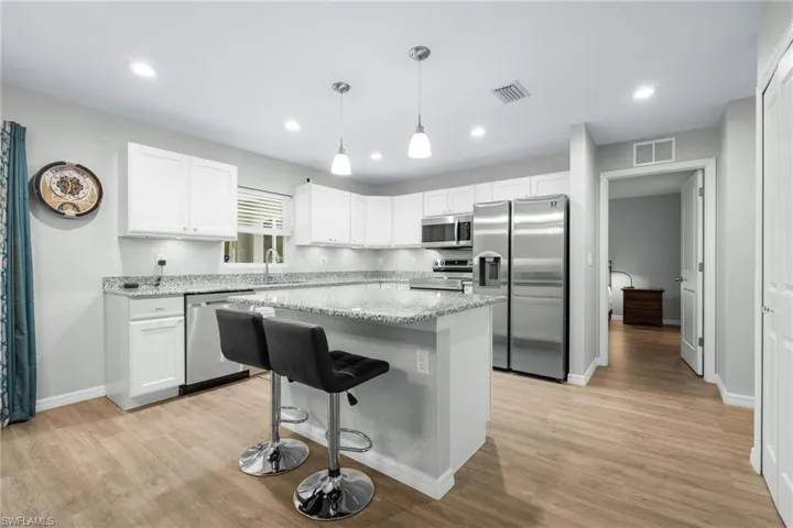 Kitchen with light wood-type flooring, stainless steel appliances, a kitchen island, and white cabinets