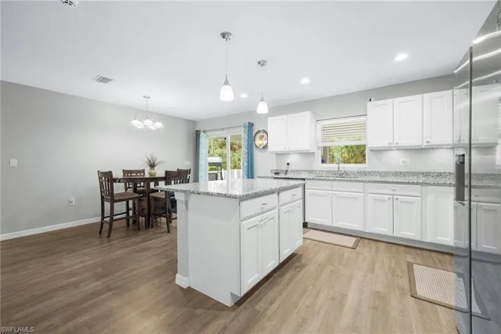 Kitchen with decorative light fixtures, light hardwood / wood-style floors, white cabinetry, and light stone countertops