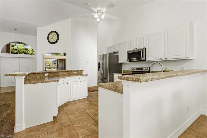 Kitchen featuring kitchen peninsula, stainless steel appliances, a high ceiling, white cabinets, and a breakfast bar area