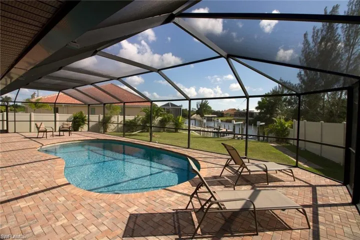 View of pool featuring a lawn, a water view, a patio, and glass enclosure