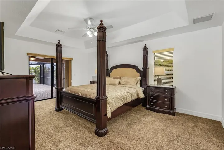 Carpeted bedroom featuring ceiling fan, a raised ceiling, and access to exterior