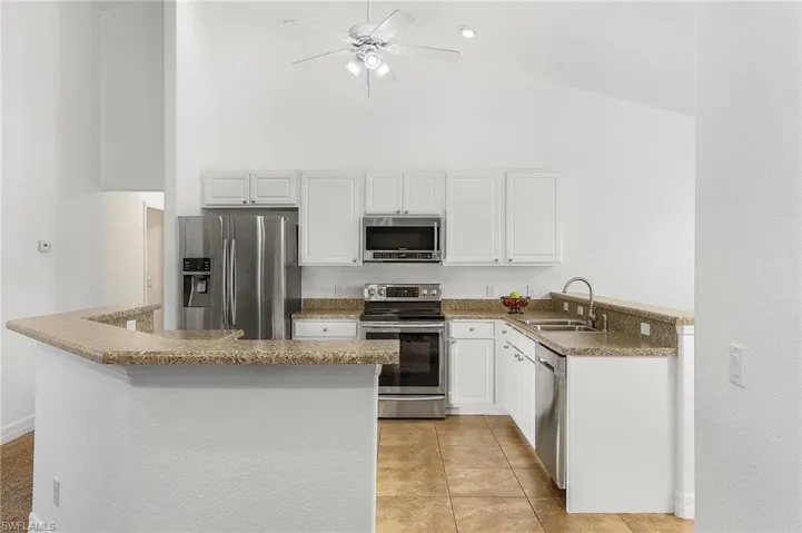 Kitchen with kitchen peninsula, stainless steel appliances, sink, light tile patterned flooring, and white cabinetry