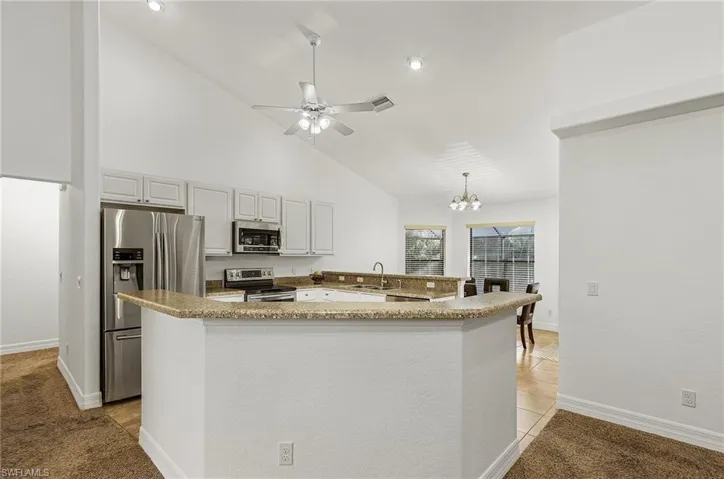 Kitchen featuring kitchen peninsula, white cabinetry, stainless steel appliances, sink, and light colored carpet