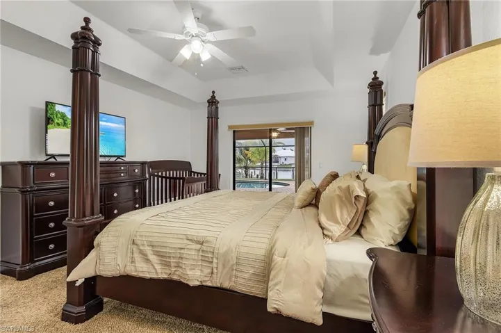 Carpeted bedroom featuring ceiling fan, a raised ceiling, and access to outside