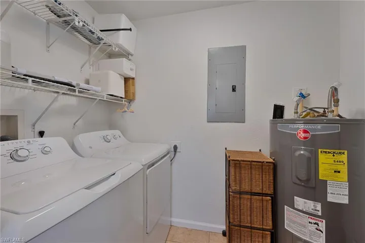 Laundry room with electric water heater, electric panel, washer and dryer, and light tile patterned floors