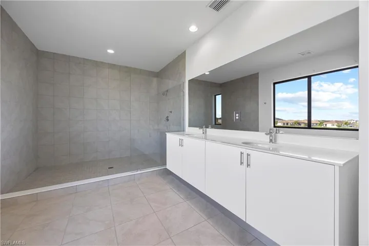 Primary bedroom featuring dual vanity sinks, modern cabinetry, quarts countertops, and luxurious shower.