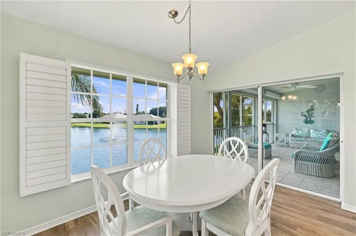 Dining space featuring wood-finish flooring, white plantation shutters, a multi-light chandelier, and sliding glass doors with access to a screened-in patio