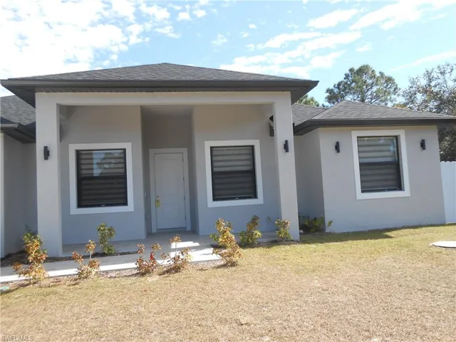 View of front of home with roof with shingles, a porch, stucco siding, and a front lawn