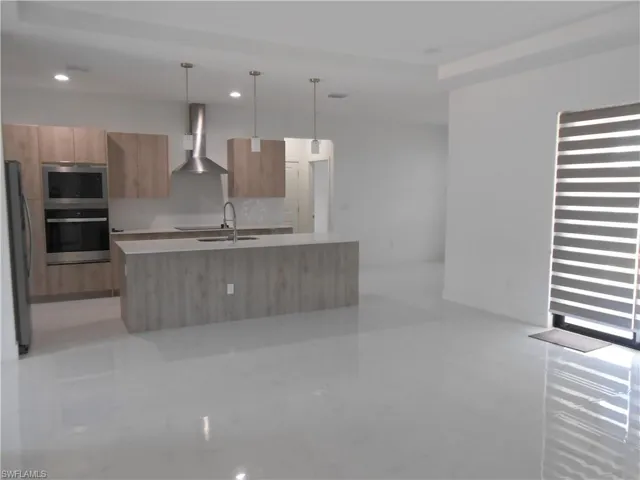 Kitchen with decorative light fixtures, stainless steel appliances, modern cabinets, an island with sink, and light stone countertops